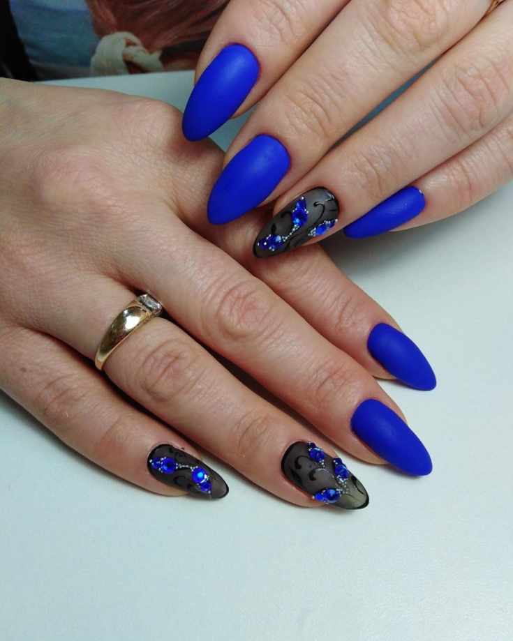 Синий матовый маникюр на длинные ногти миндаль с полупрозрачным черным цветочным дизайном и синими стразами